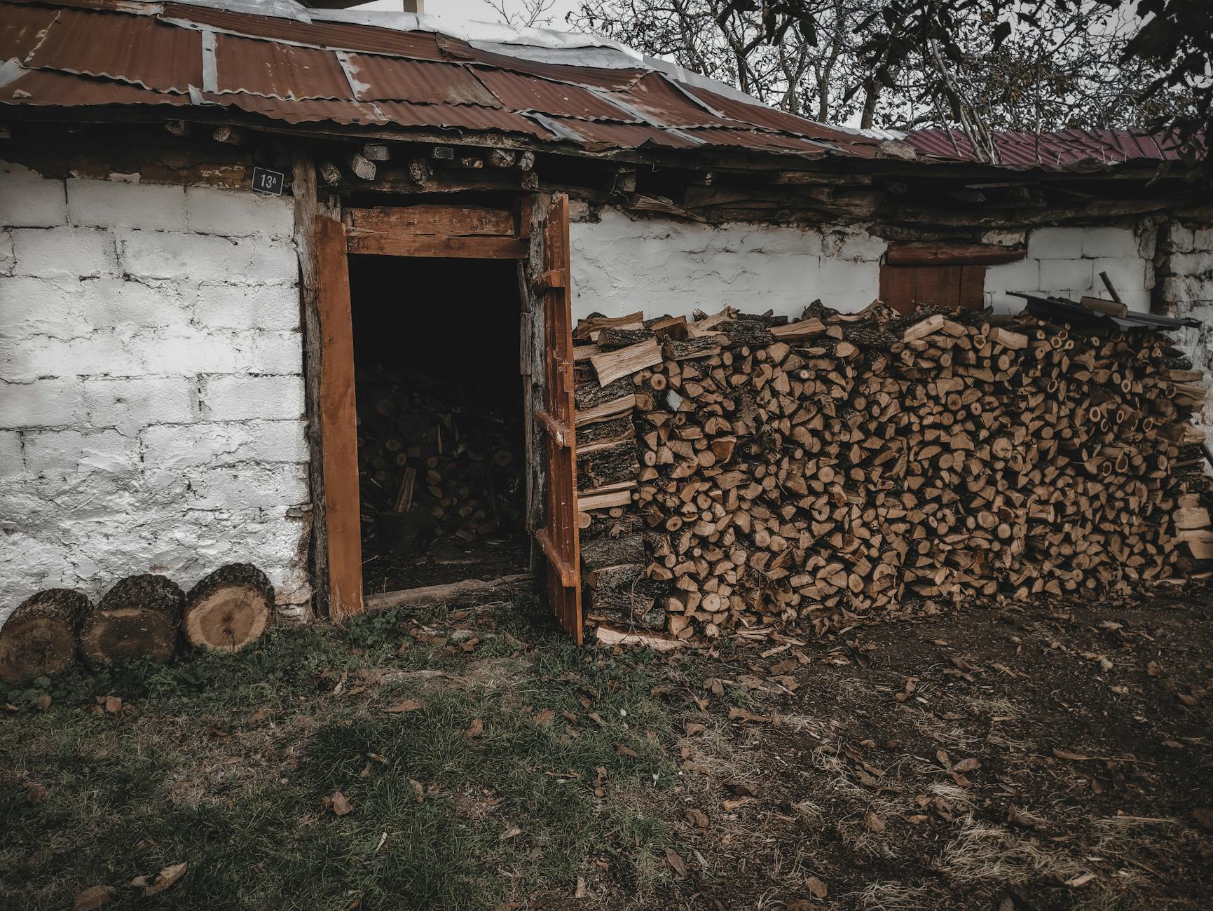 Stos ułożonego drewna opałowego przy otwartych drzwiach szopy