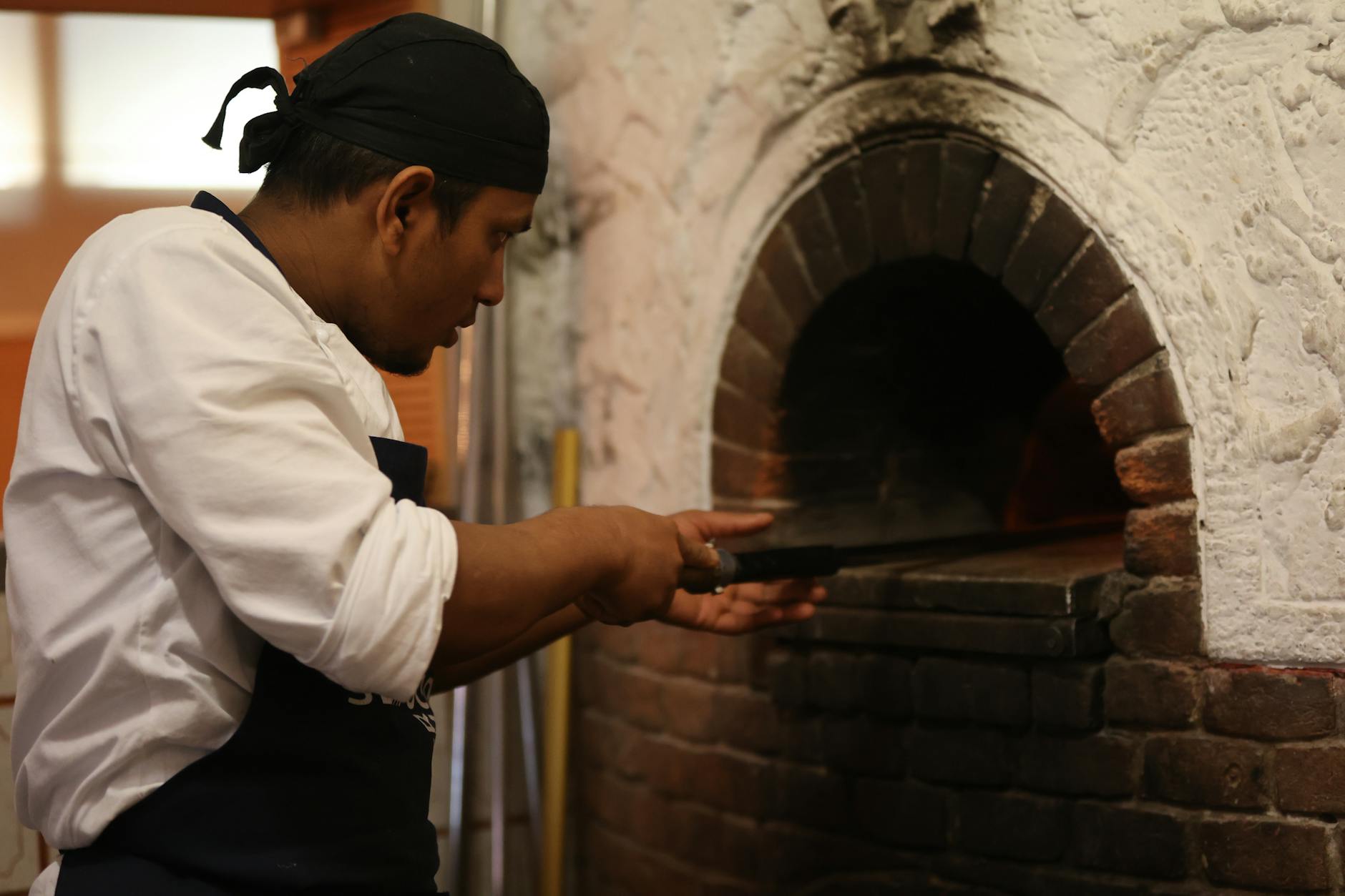 Kucharz wsuwający pizzę łopatą do murowanego pieca w pizzerii