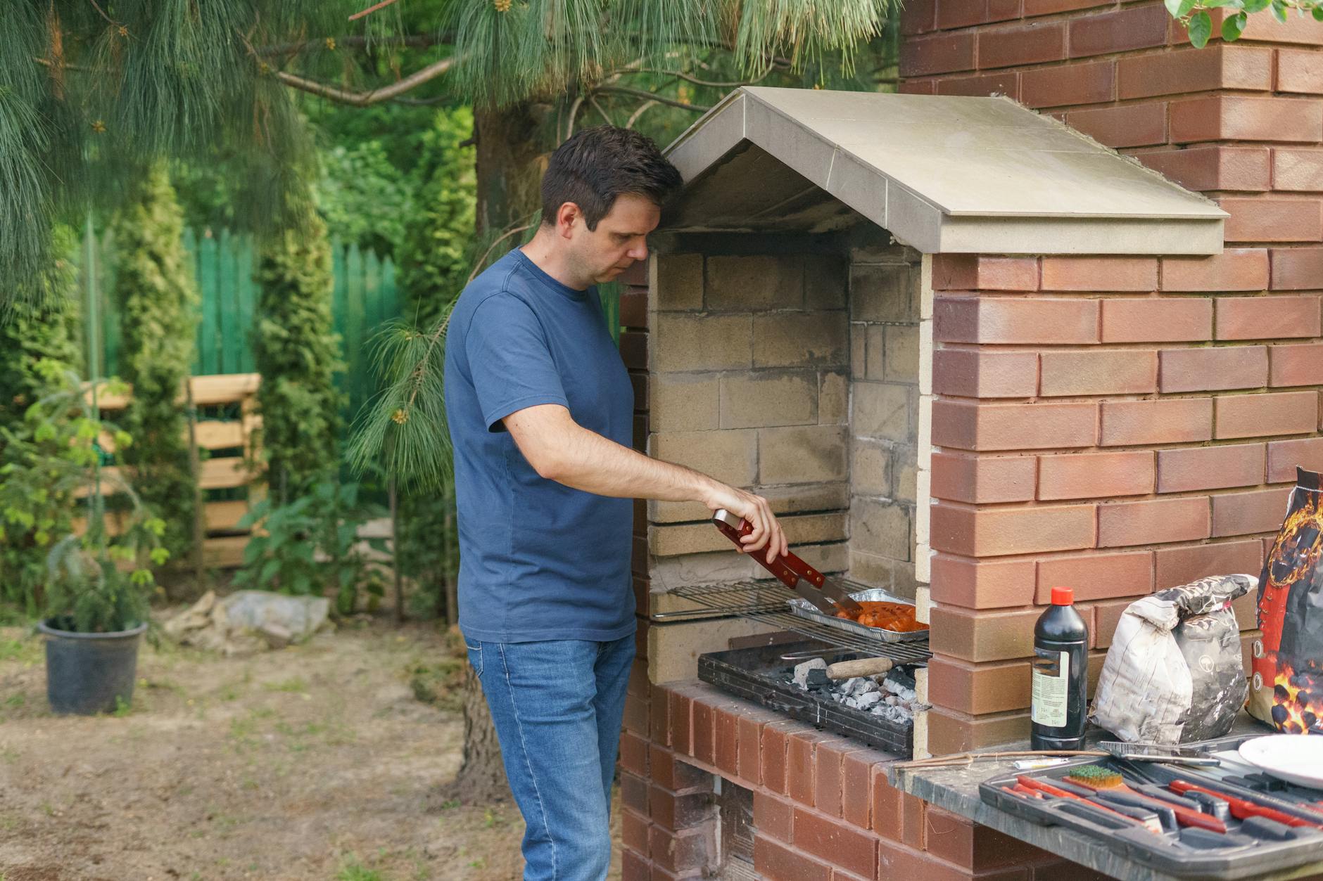 Mężczyzna grilluje mięso w ogrodzie na murowanej grillowędzarni