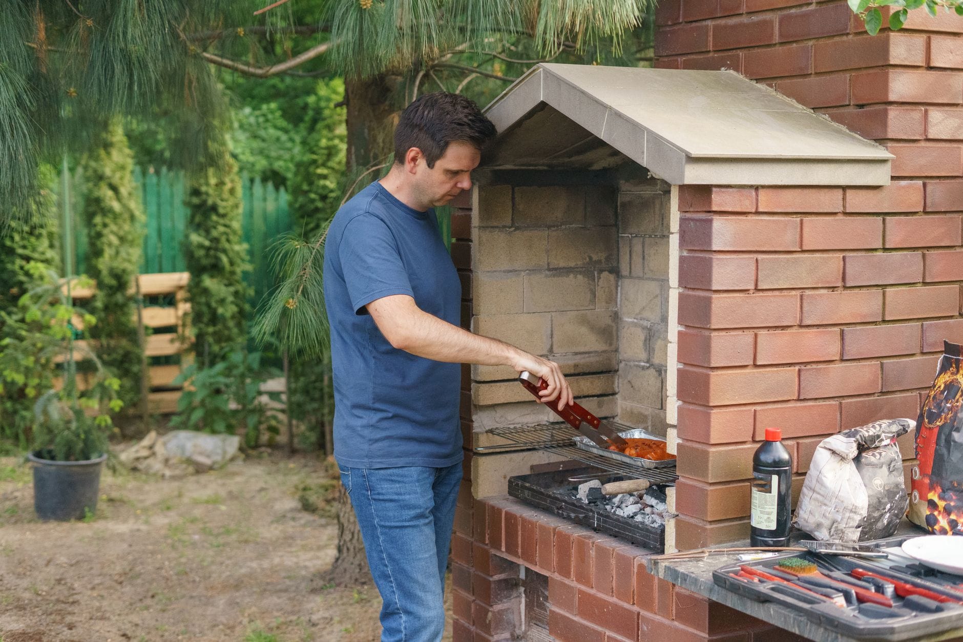 Mężczyzna grilluje mięso na murowanym grillu w ogrodzie