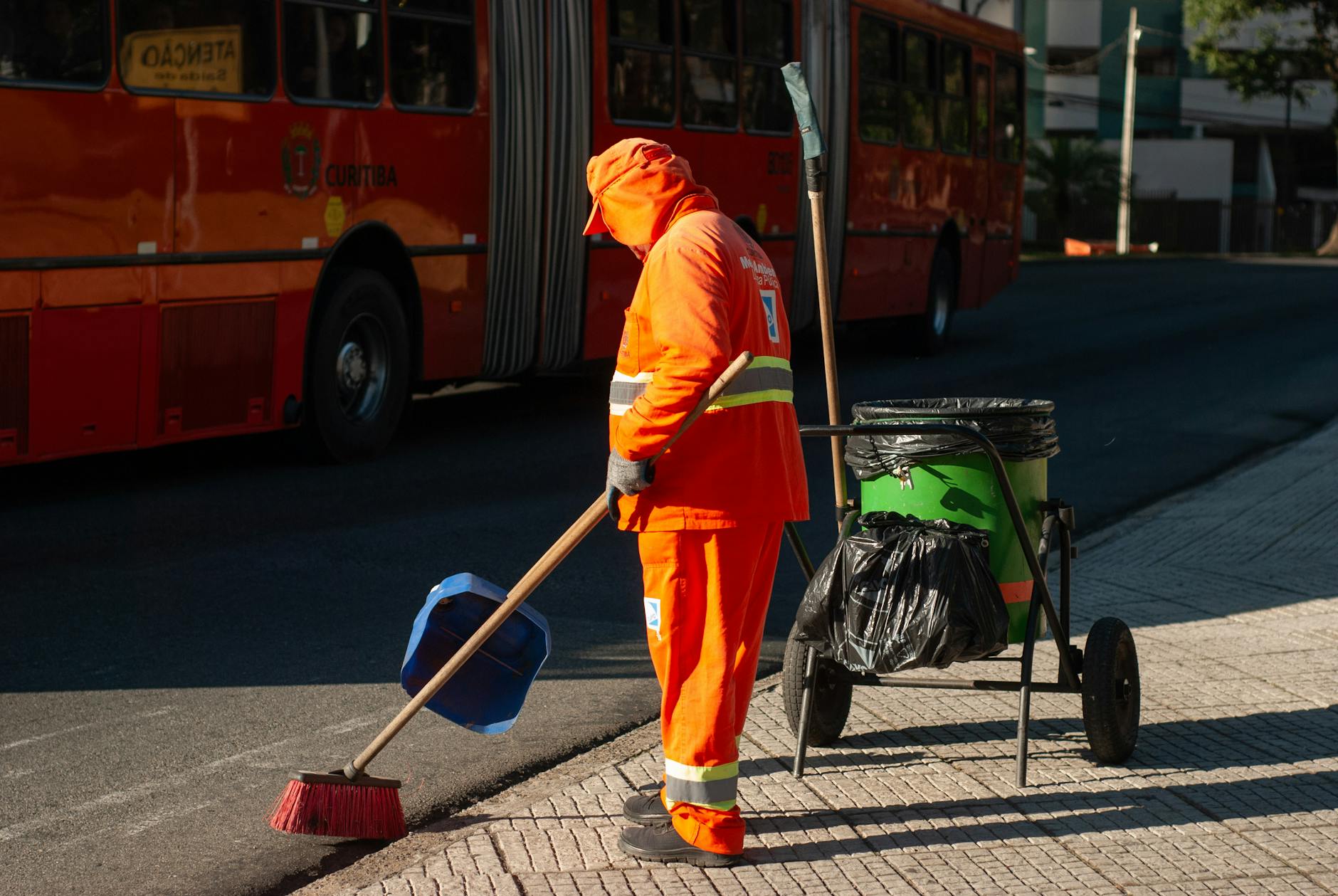 Pracownik w pomarańczowym stroju zamiata chodnik obok autobusu miejskiego